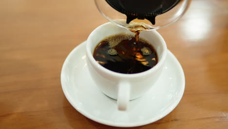 pouring drip coffee from glass server to white cup on sauce