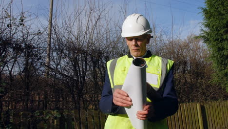 a mature architect builder looking at building plans and blueprint on a construction site wearing hard hat