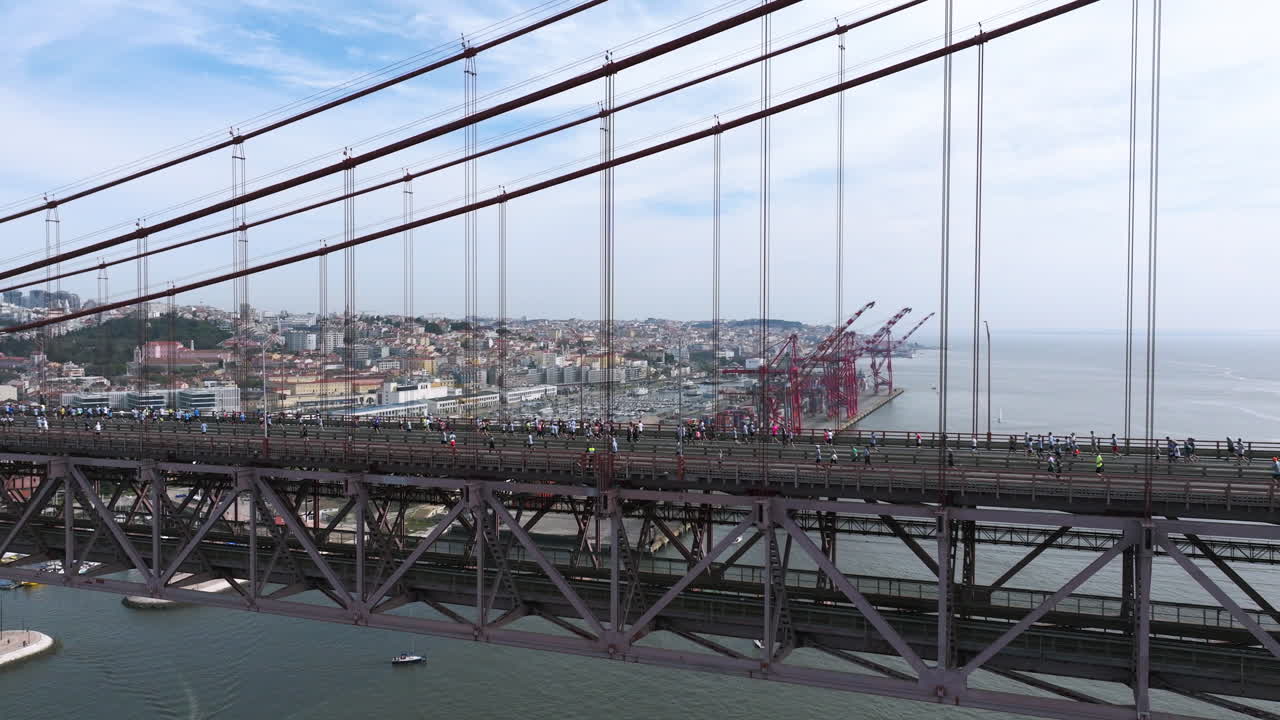 Half marathon and 10K long distance running event in Lisbon, Portugal, Europe. Runners crossing the iconic famous red 25th April suspension bridge. Slow panning aerial drone shot