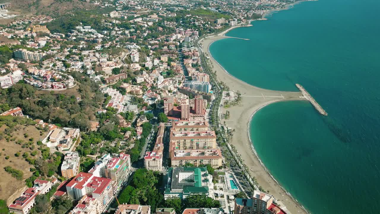 High altitude drone over Playa de la Malagueta in Málaga, Spain. Capturing calm beach, turquoise sea, and sunlit cityscape on a bright sunny day