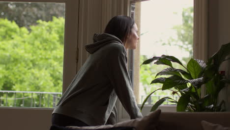 woman in lounge at home walking across room to window and looking out