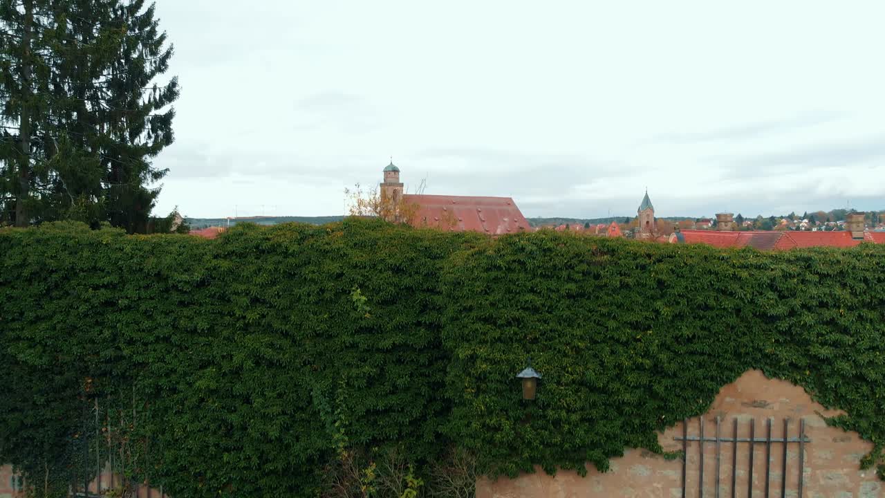 un panorama di una città storica e il drone inizia a scendere a cascata lungo la cinta muraria poi scende lungo un muro vivo di una pianta