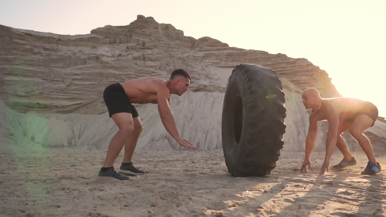 dos atletas entrenan en modo activo en la playa haciendo flexiones y empujando una gran rueda