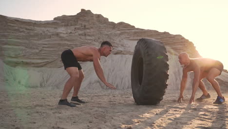 two athletes train in active mode on the beach doing push-ups and pushing a huge wheel