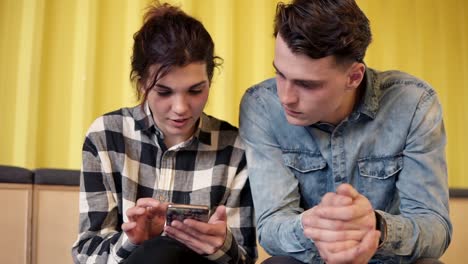 A-couple-sitting-and-chatting-about-something.-Young-attractive-girl-shows-her-boyfriend-something-on-her-smartphone.