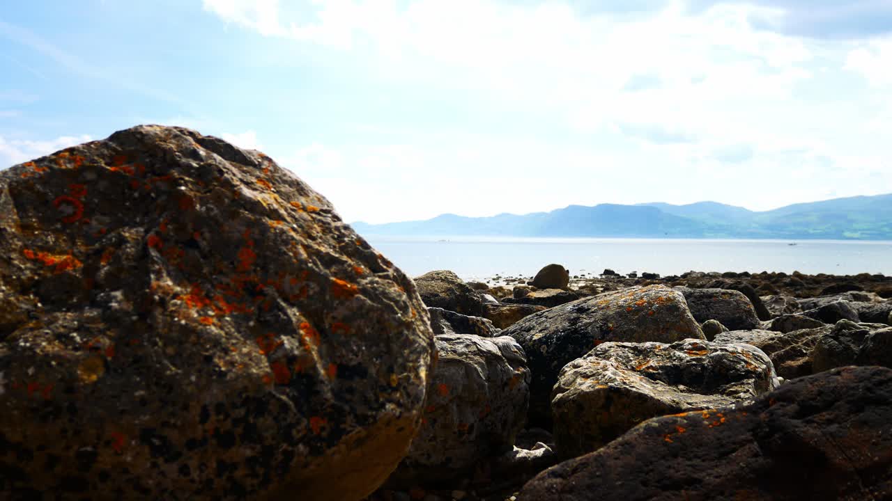 Farverigt strandlandskab med store sten under bjergkæden i Nordwales, sænkende kranarm til højre.