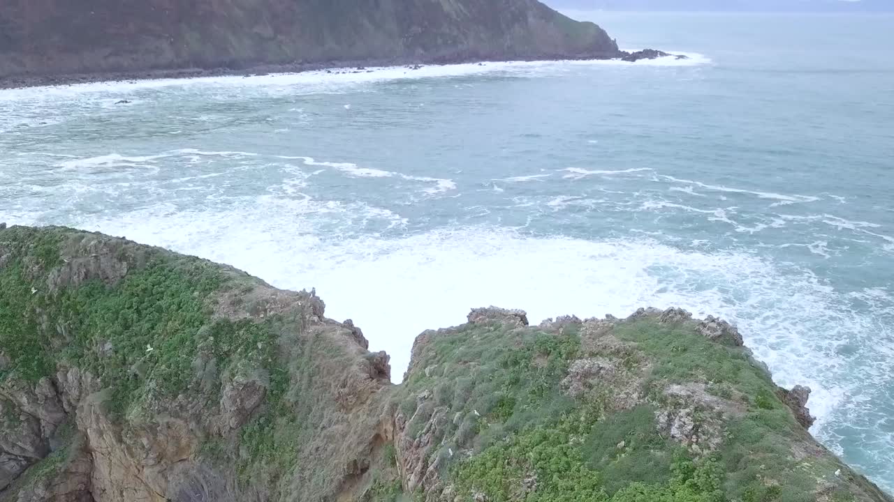 Drone footage of a rocky island with crashing waves at a cliff