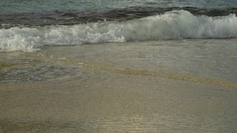 cámara lenta de una ola rompiendo en la playa de arena, ángulo bajo