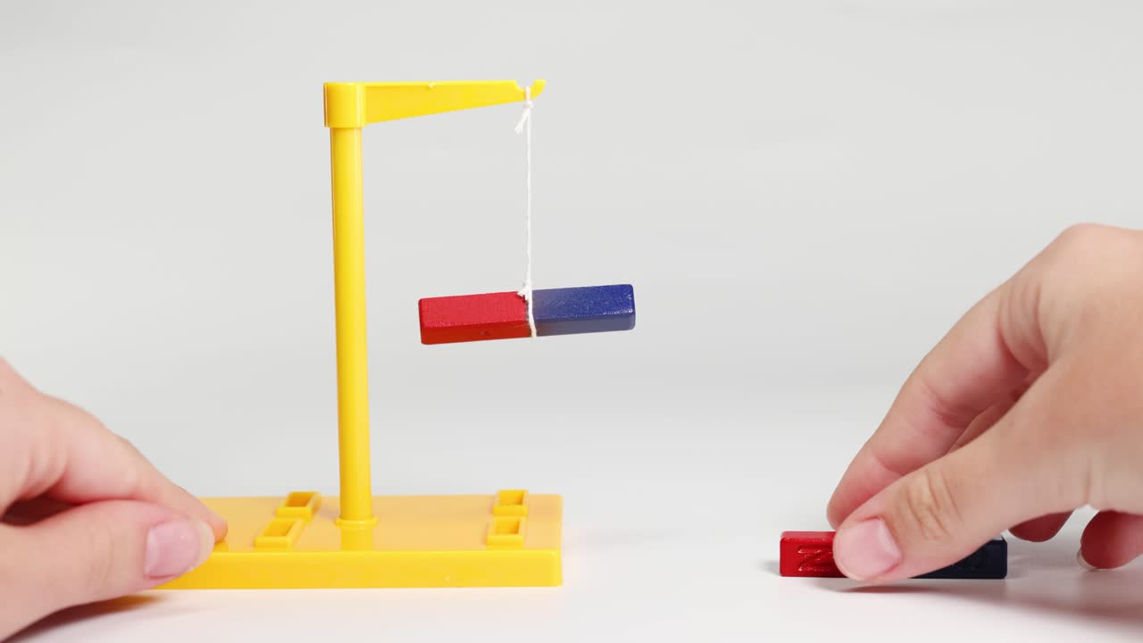 Hands manipulate magnets on a stand, illustrating magnetic attraction and repulsion. Bright lighting, simple setup, educational focus