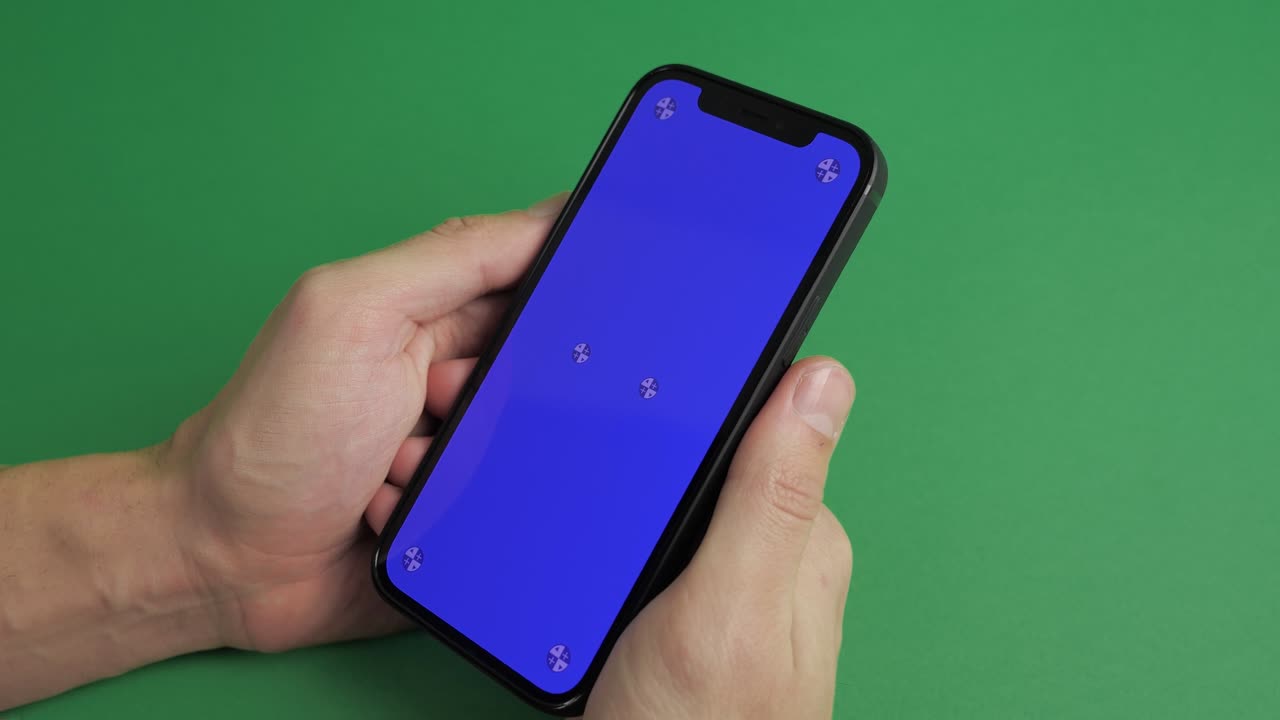 primer plano de mano masculina sosteniendo teléfono móvil con pantalla azul vertical clave de croma tecnología de teléfono inteligente teléfono celular pantalla de mensaje táctil mano en fondo de pantalla verde.