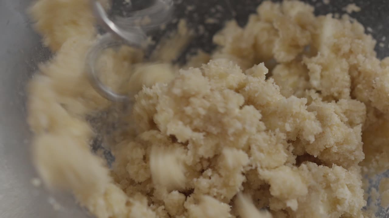 Slow motion Hand mixer blending cookie dough mixture inside glass bowl