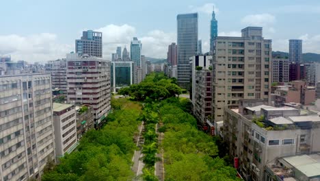 Aerial-flyover-famous-greened-Renai-avenue-with-trees-and-traffic-in-Taipei-city,-Taiwan---Skyline-of-Taipei-in-background