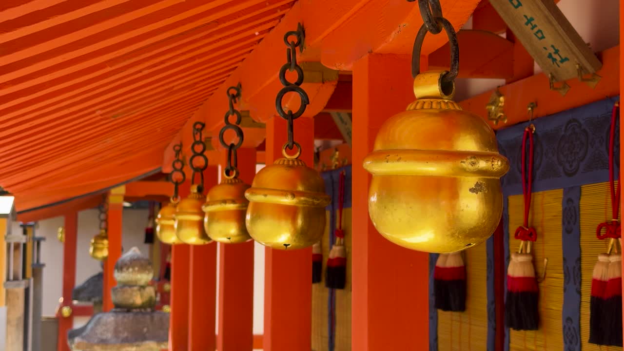 Rækker af gyldne messingklokker hænger fra cinnoberrøde træbjælker ved en japansk Shinto-helligdom