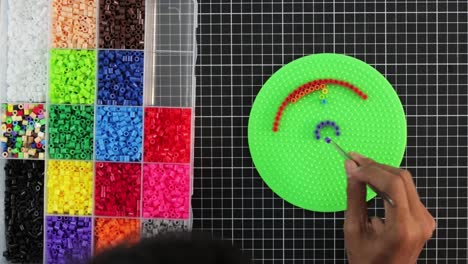 colorful beads on pegboard for craft activity, hand creating a pattern, timelapse