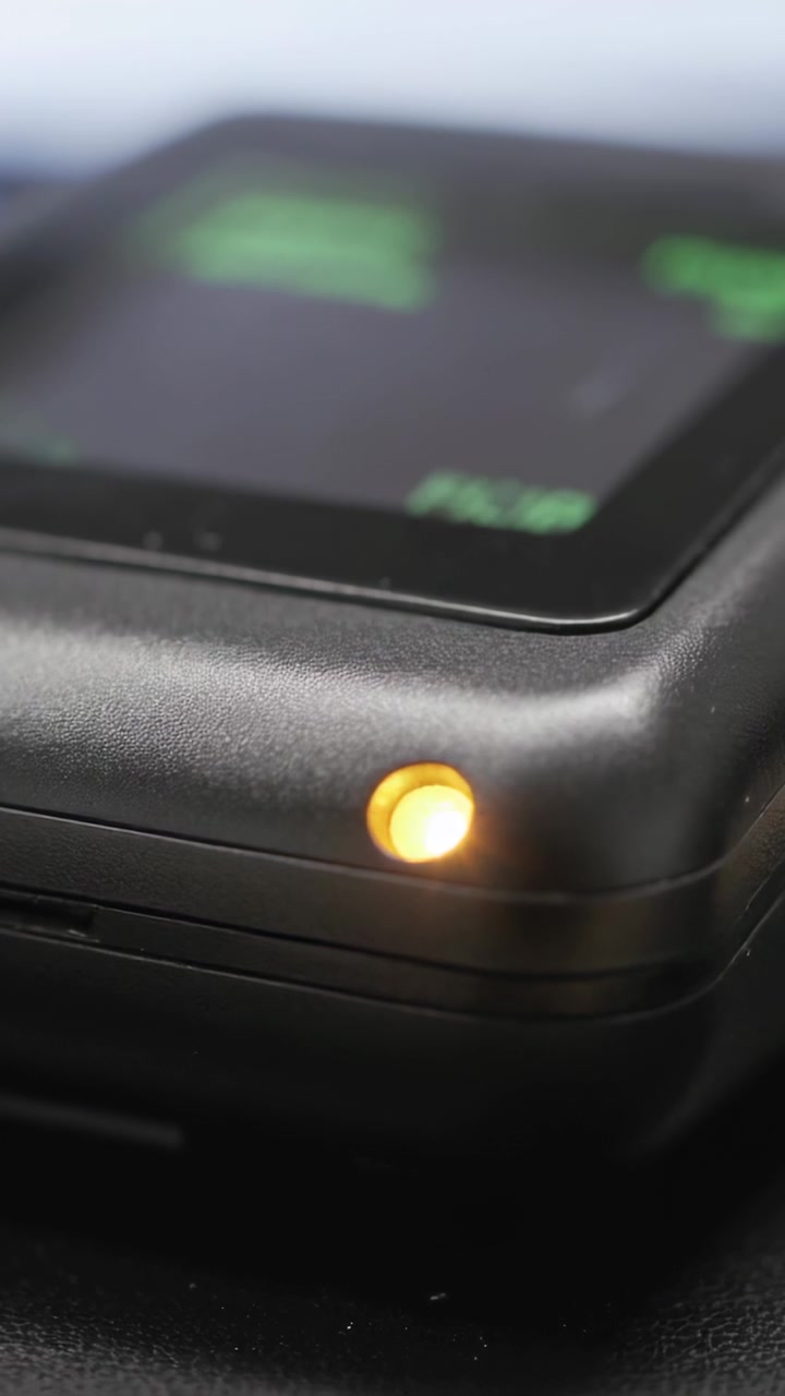 Video verticale: Un dispositivo nero riceve alimentazione e si accende su una scrivania, mostrando un LED ambra e un'interfaccia utente verde.