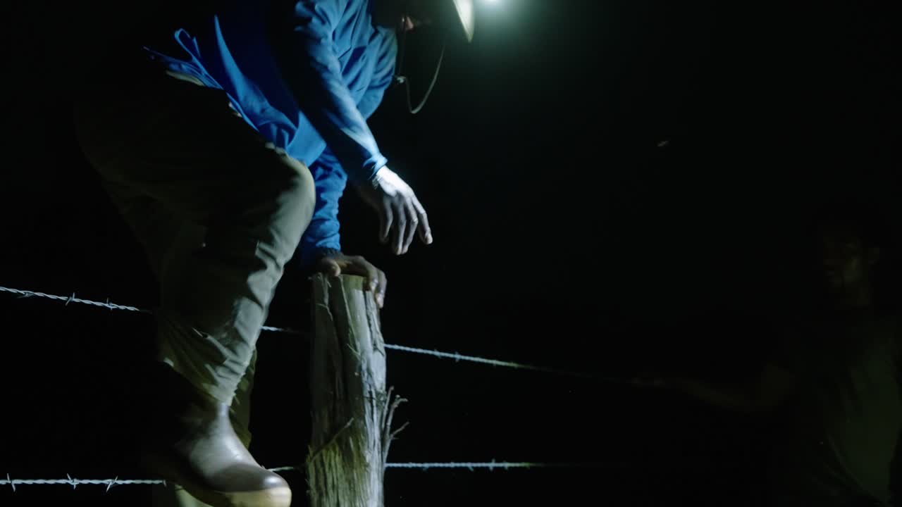 hombre afroamericano en viaje de caza saltando sobre una cerca de alambre de púas con lámpara de cabeza en medio de la noche