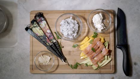 Display-of-ingredients-for-Sushi-with-falling-fresh-green-herbs-seen-from-top-down-on-kitchen-counter-with-bowls-of-ingredients-including-rice,-salmon-and-fruits-ready-to-make-Sushi