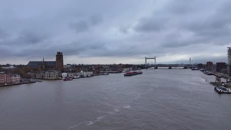 In-Der-Ferne-Die-Silhouette-Eines-Containerschiffs,-Das-An-Der-Stadt-Dordrecht-Vorbeifährt