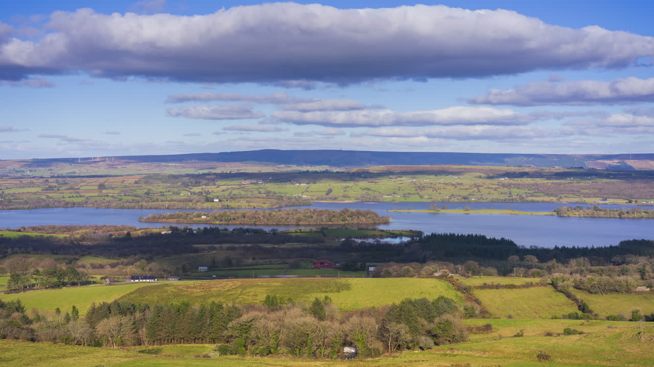 Timelapse di campagna rurale con colline, boschi misti e un lago in lontananza durante una giornata primaverile soleggiata e nuvolosa, vista da Carrowkeel nella contea di Sligo in Irlanda
