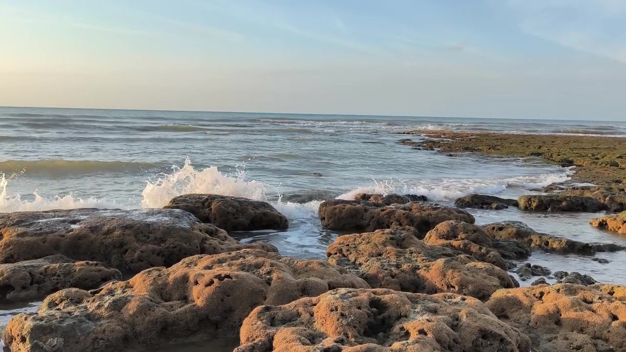 Onde dell'oceano che si infrangono contro una costa rocciosa al tramonto