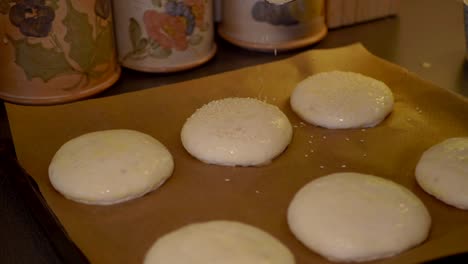 Una-Mujer-Rociando-Semillas-De-Sésamo-Encima-De-Los-Bollos,-Preparándolos-Para-El-Horno