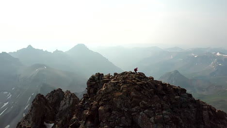 female climber on top of rocky summit, dynamic aerial view