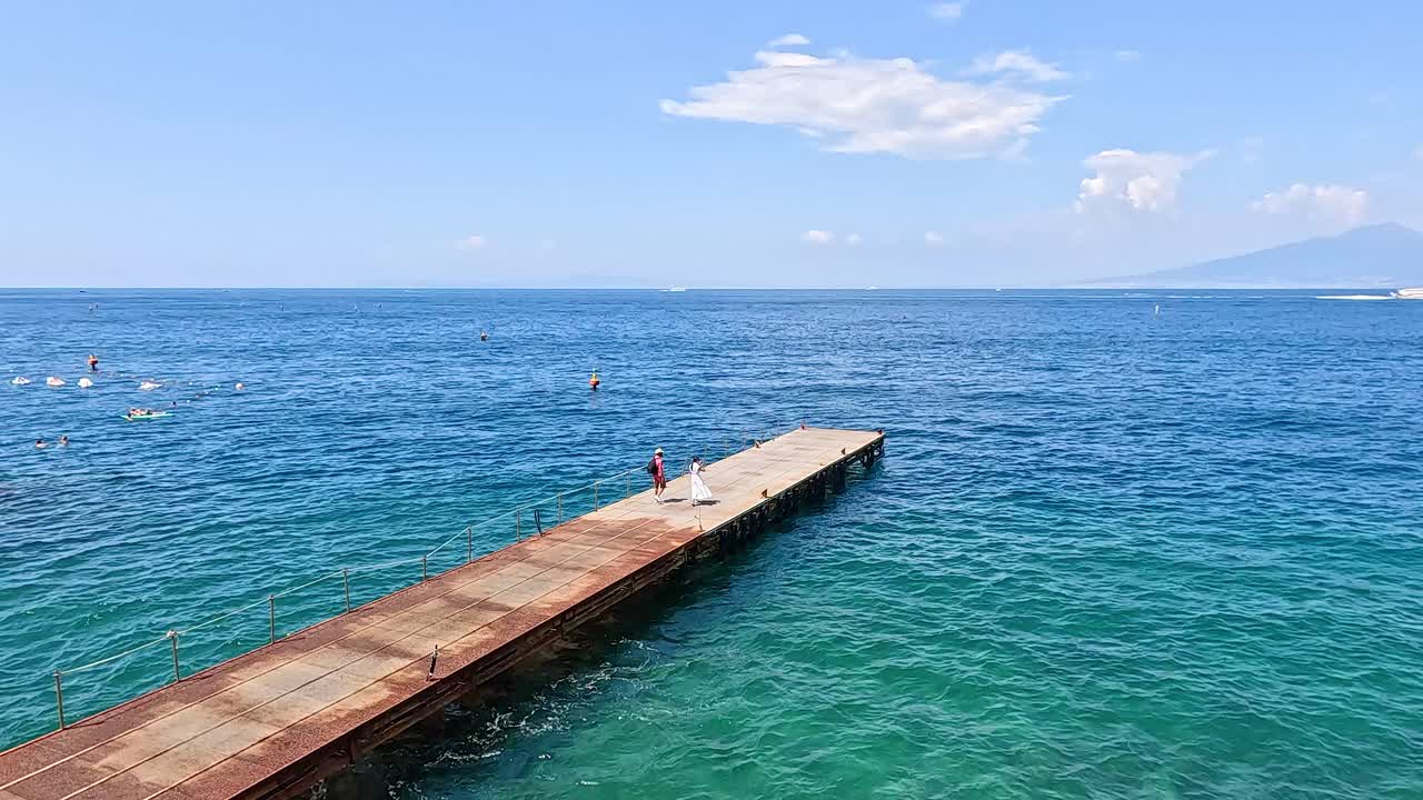 Individual strolling on pier over clear blue water