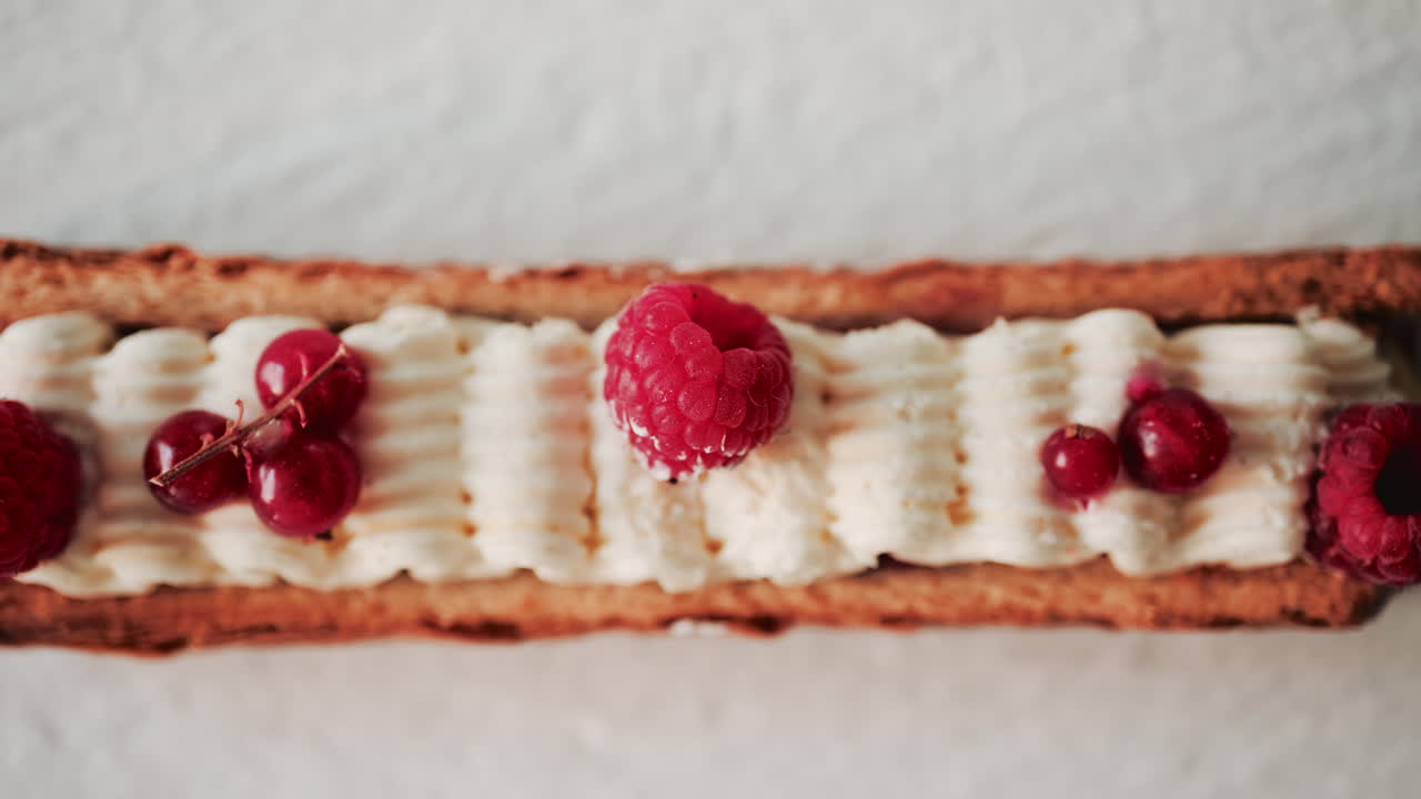 Close up of a gourmet pastry topped with cream, raspberries, and red currants