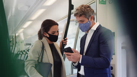 business commuters stand in train carriage with mobile phones wearing ppe face masks during pandemic