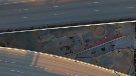 Top-down-aerial-shot-of-a-skatepark-wedged-between-highways-at-sunrise