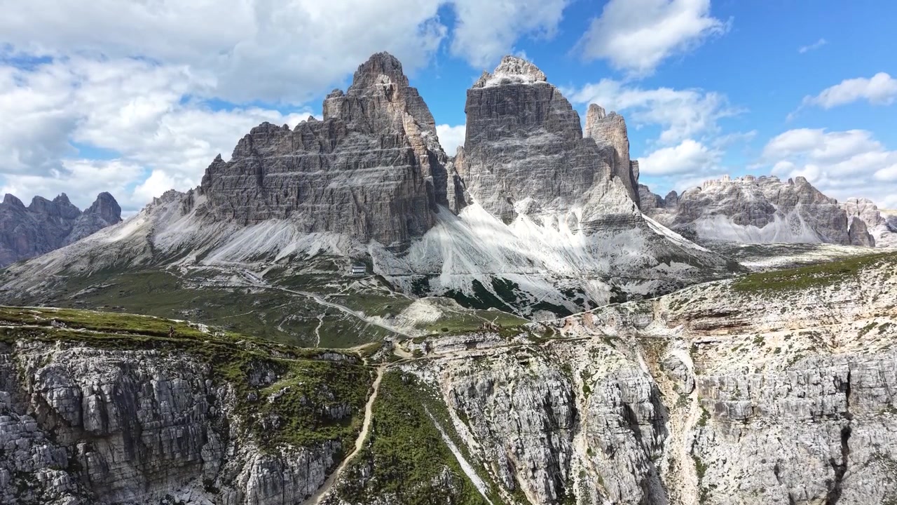Rivelazione lenta verso l'alto con drone delle iconiche Tre Cime di Lavaredo che emergono sopra aspre scogliere calcaree nelle Dolomiti, Italia