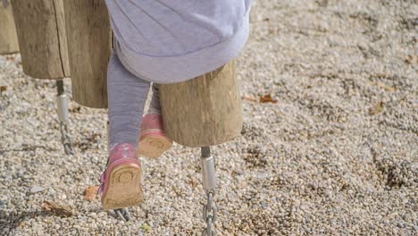 Vista-De-Las-Piernas-De-Un-Niño-Pequeño-Balanceándose-En-Un-Asiento-De-Madera-En-El-Patio-De-Recreo