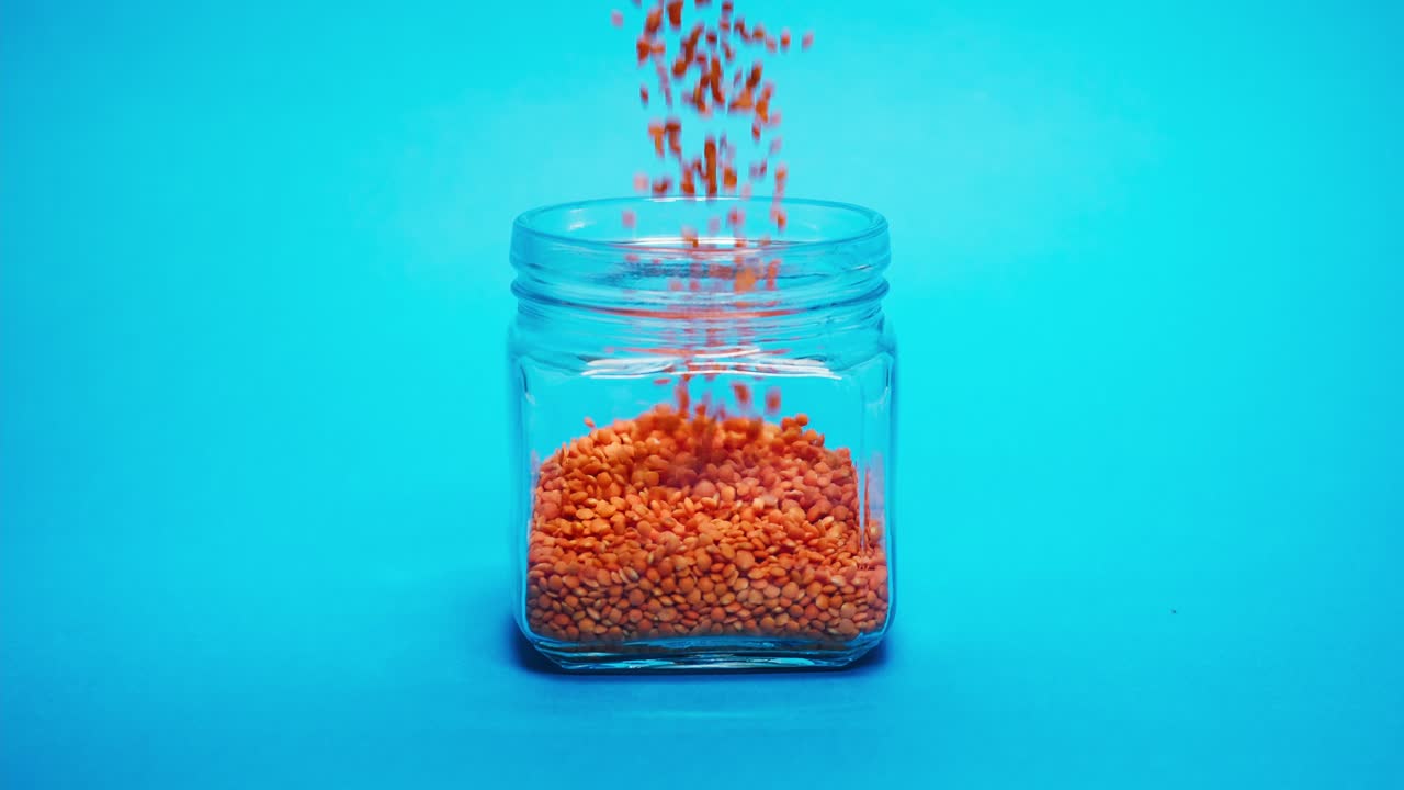 Red Lentils Falling and Filling a Clear Glass Jar