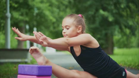 a focused young girl demonstrates flexibility and strength through a yoga pose while practicing on a path surrounded by lush greenery and natural light