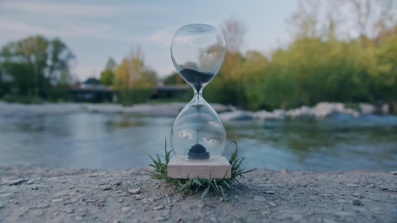 reloj de arena en la naturaleza con tráfico de fondo y personas en reflejo