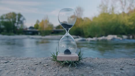 hourglass in nature with traffic in background and people in reflection