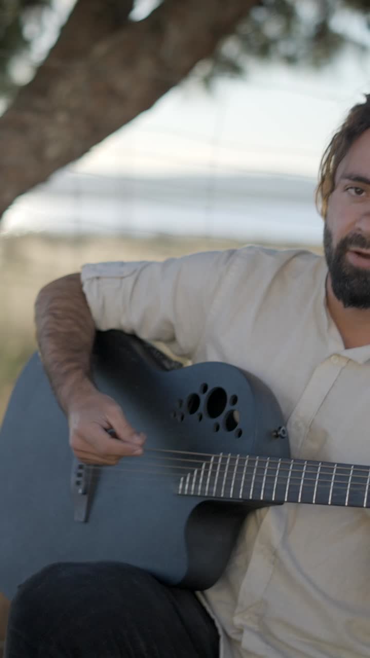 Mann spielt Akustikgitarre und singt im Freien
