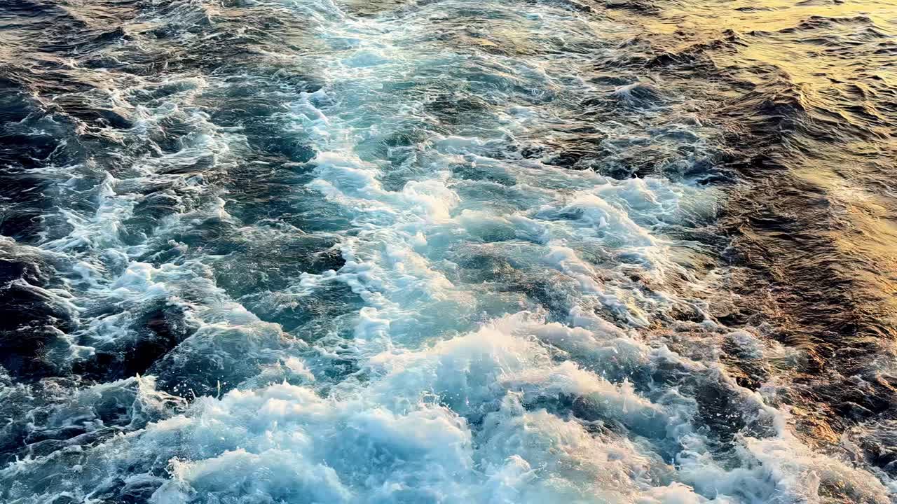 Vista dall'alto di una potente scia di acqua bianca dietro una grande nave sulla superficie di un oceano estivo di un blu profondo al tramonto, con riflessi dorati e bolle schiumose turbolente create dall'elica del motore