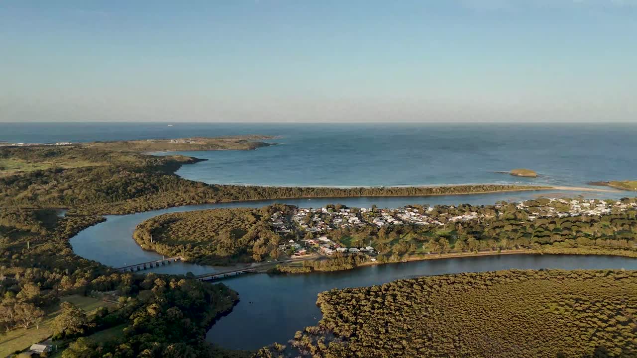 Aerial establishing pullback above Minnamurra, Australia, featuring coastal village with sweeping ocean and town views
