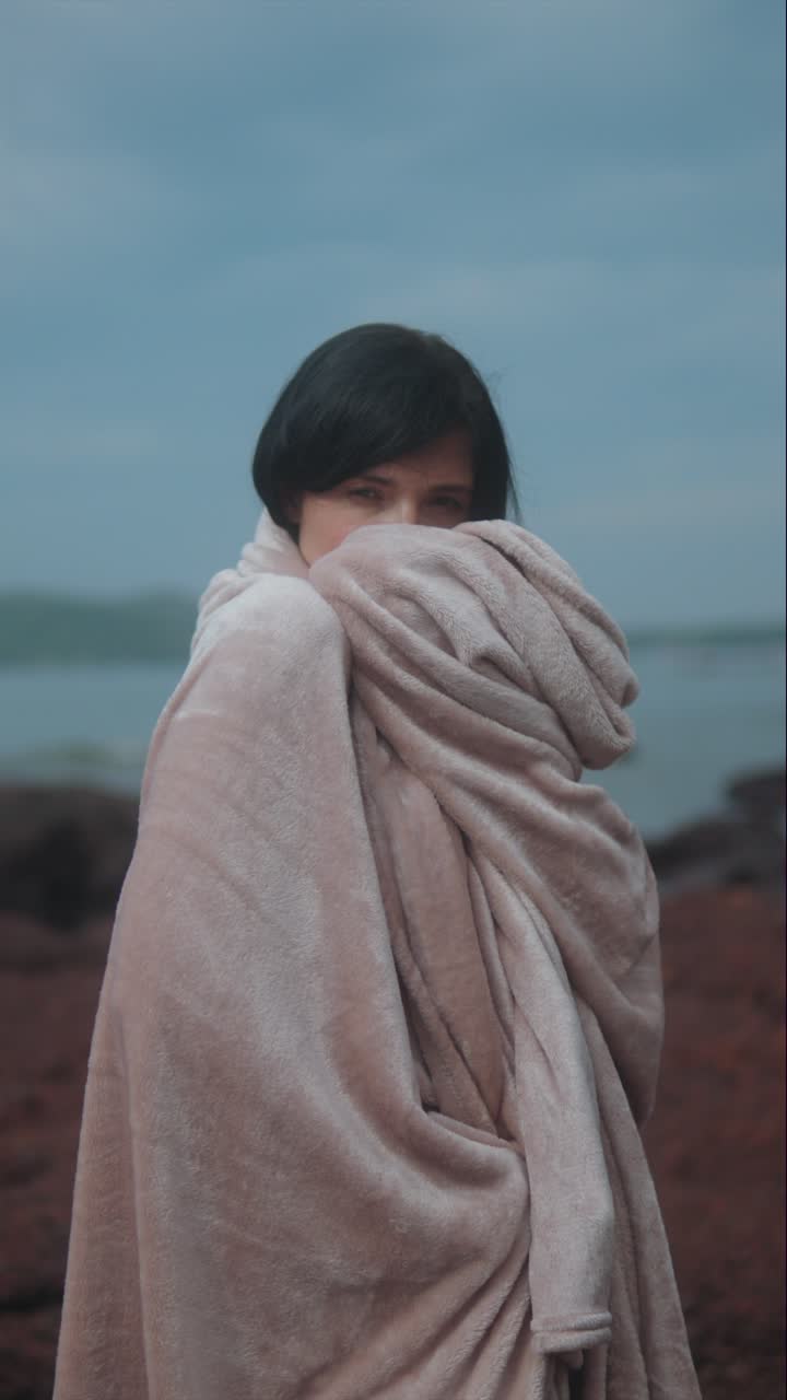 Retrato vertical de mulher embrulhada em cobertor perto do oceano