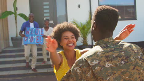 familia de varias generaciones con padres y esposa dando la bienvenida a un soldado del ejército a casa de licencia con una bandera