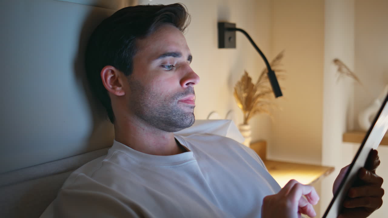 Home guy reading tablet information surfing internet in bed closeup. Man working