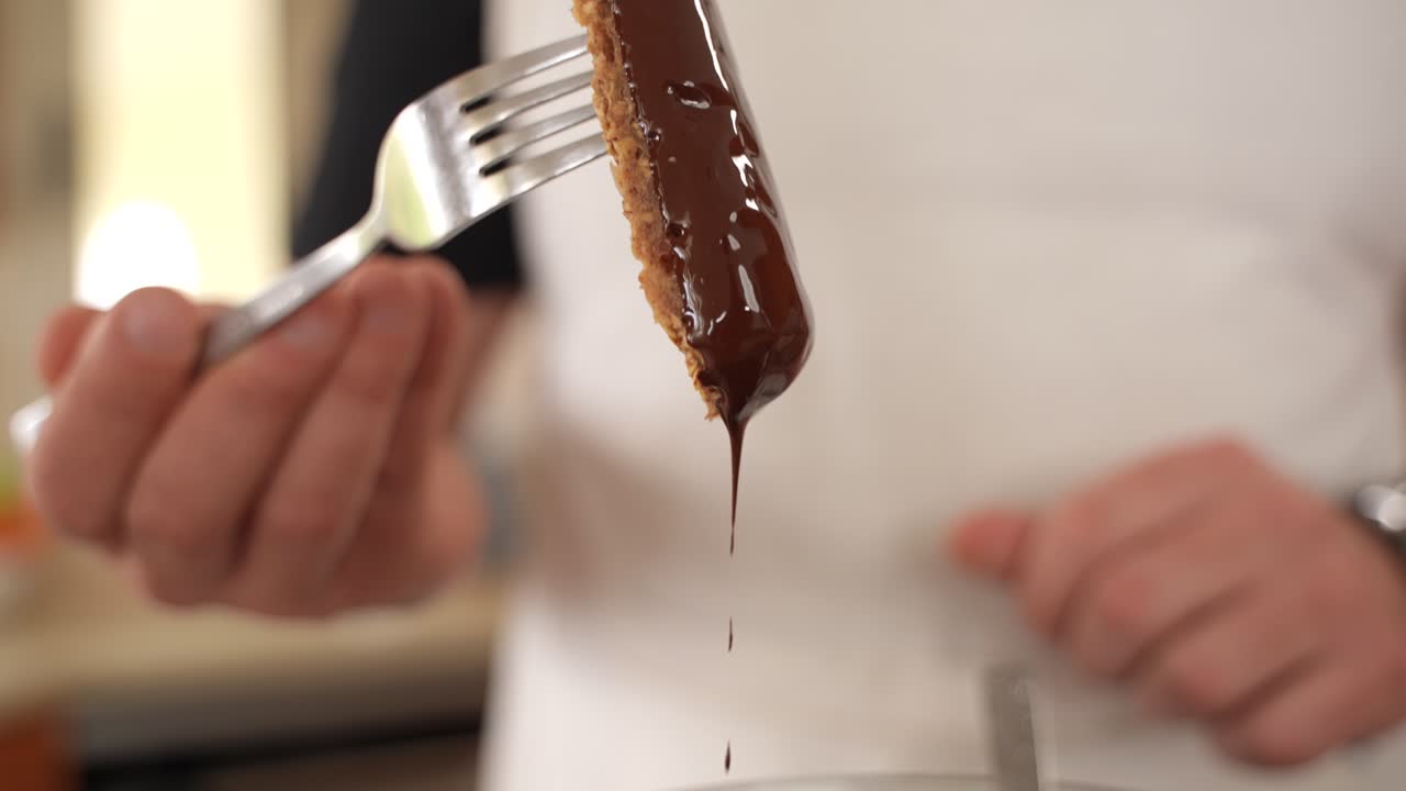 흰 셔츠를 입은 요리사가 포크에 있는 오트밀 바를 흔들고 초콜릿이 슬로우 모션으로 떨어지는 모습