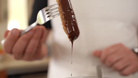 chef con camisa blanca sacude barra de avena con tenedor, chocolate goteando en cámara lenta