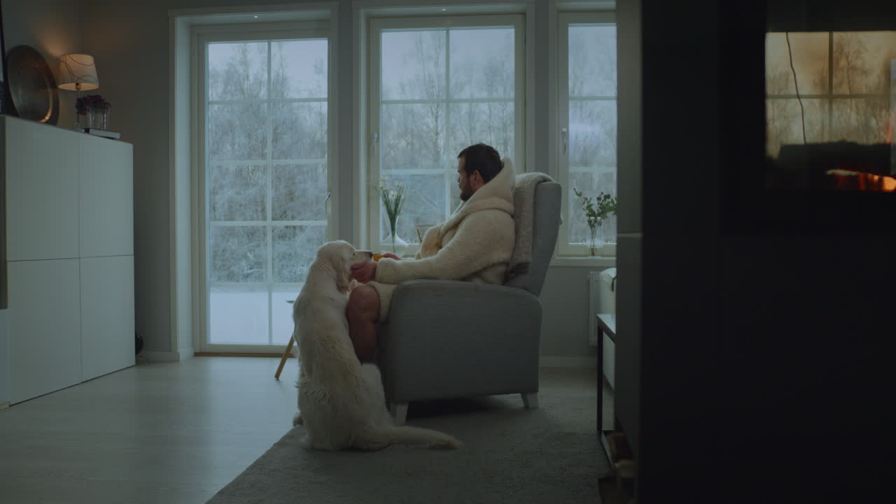 Man and dog warming up indoors near fireplace in harsh cold winter. Handheld