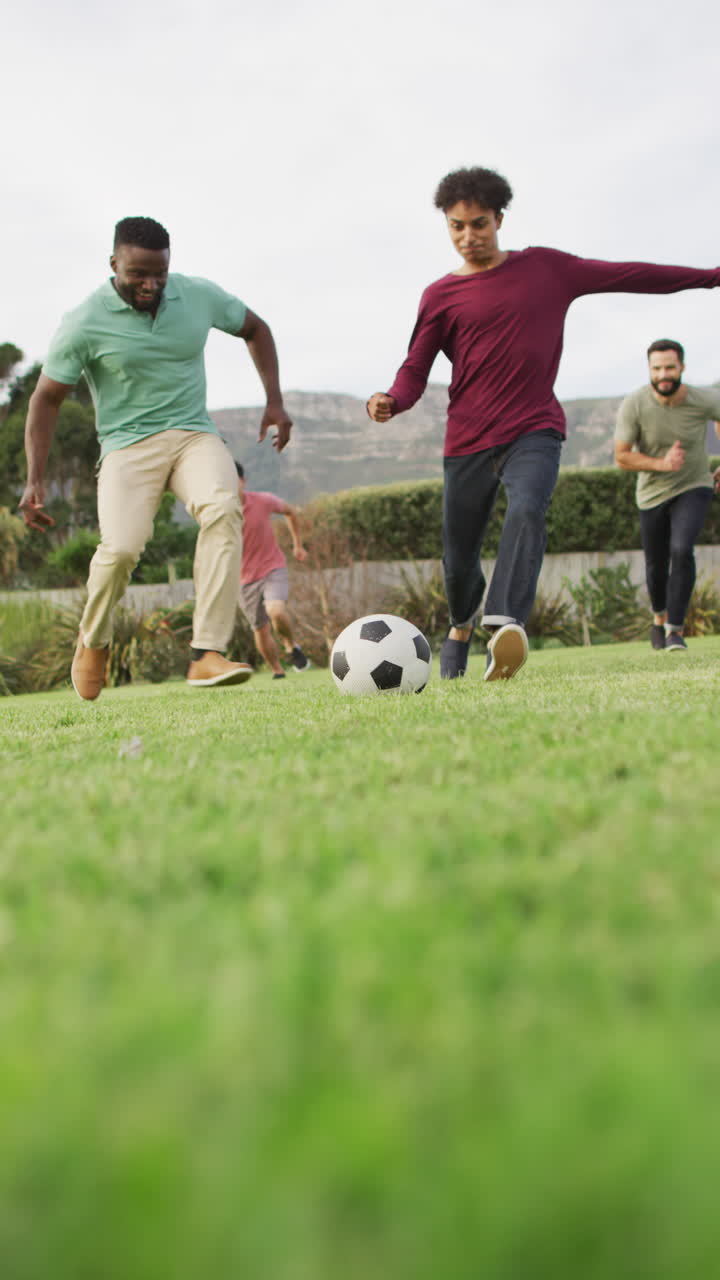 video vertical de amigos varones felices y diversos jugando al fútbol en el jardín