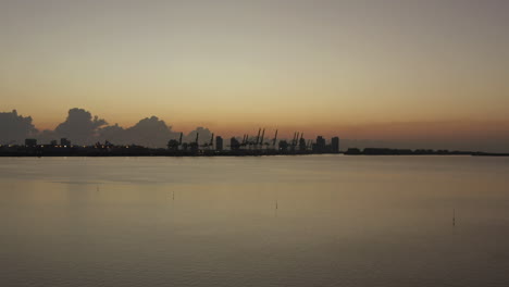 aerial view silhouette miami shipping port cranes on coastal horizon during sunset