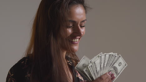 studio shot of excited woman celebrating winning cash prize holding handful of 100 dollar bills 1