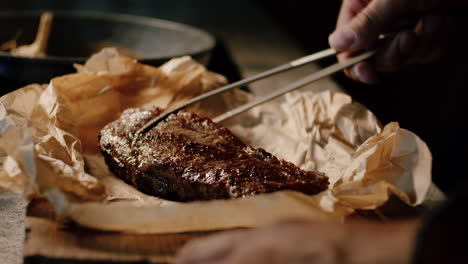 seared steak with caramalized crust being placed on paper with tongs, slowmo