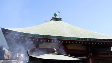 el humo se extiende a través de un techo de estilo pagoda contra el cielo azul.